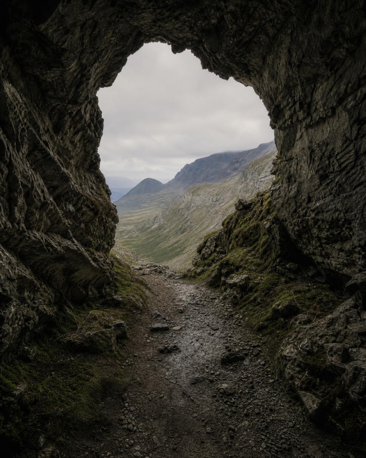 Walking path through a limestone cave toward a mountain valley
