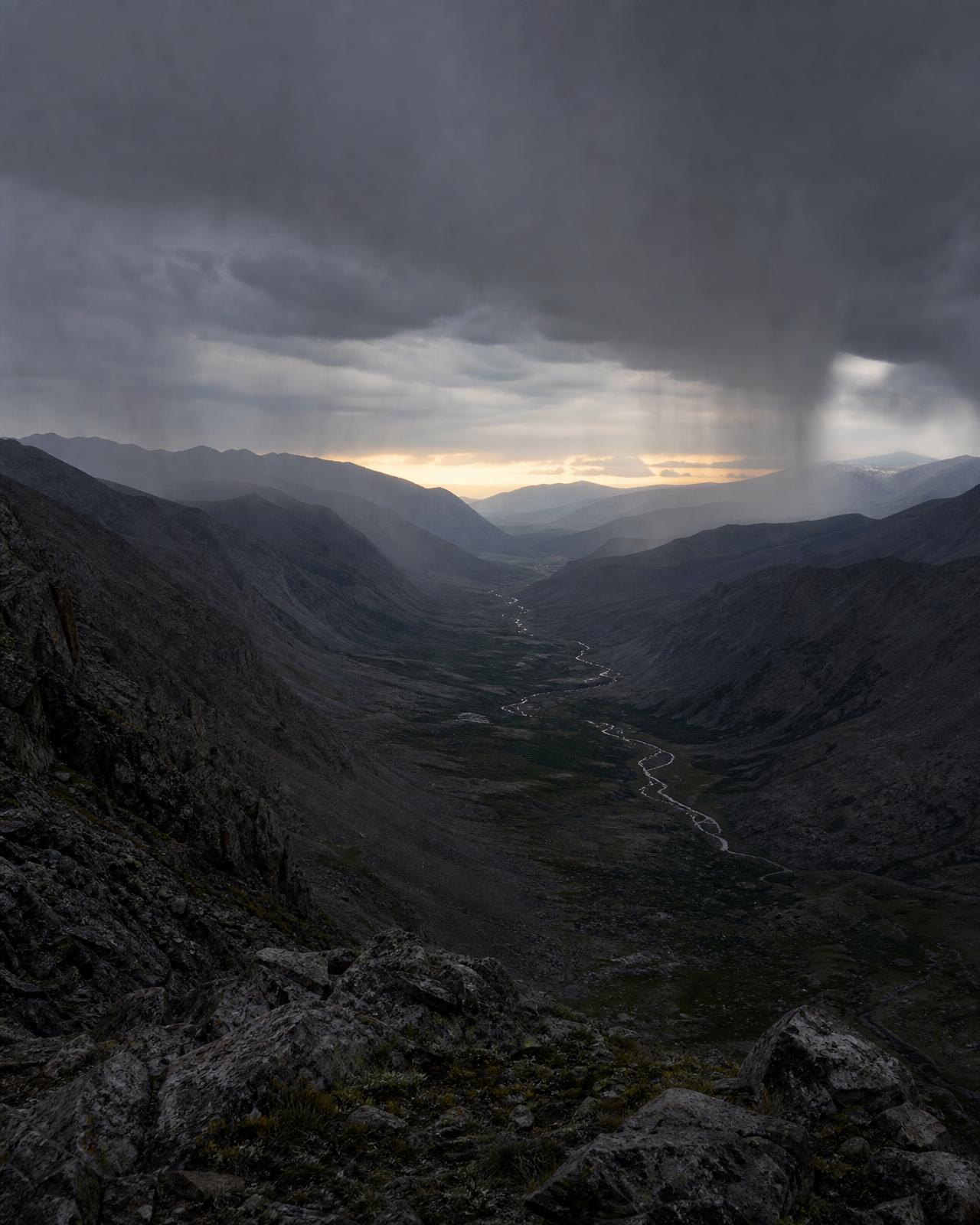 Rain falling across a dark mountain pass at dawn