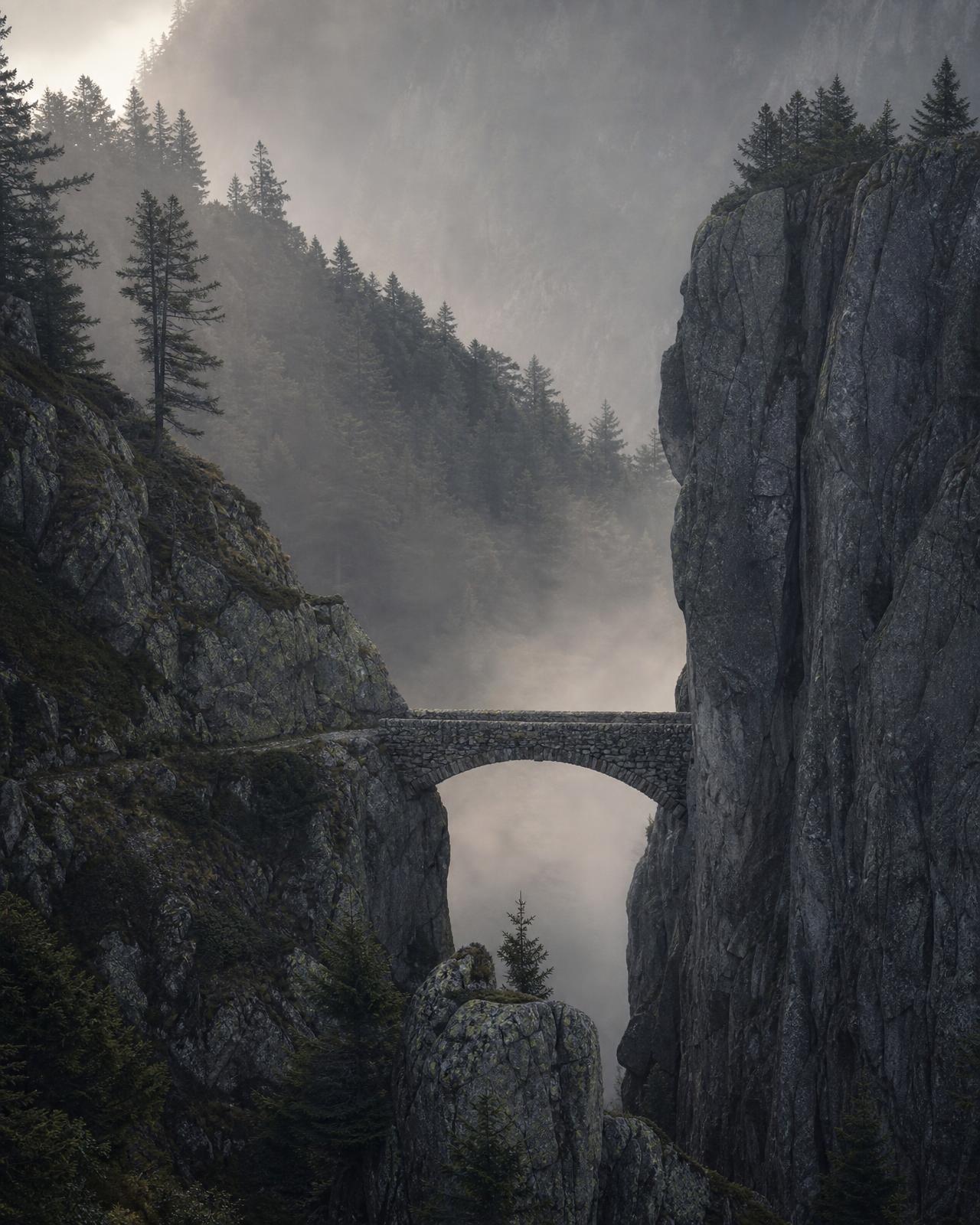 Old stone footbridge spanning a remote mountain gorge in morning mist